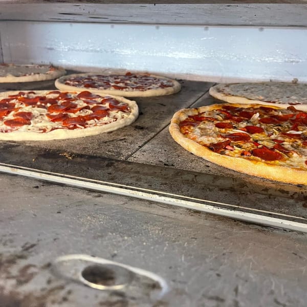Multiple Antonella's Pizzeria pizzas, some raw and some cooked, baking inside a large oven.