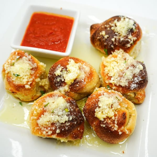 Antonella's Pizzeria garlic knots, topped with parmesan cheese and herbs, served with marinara sauce.
