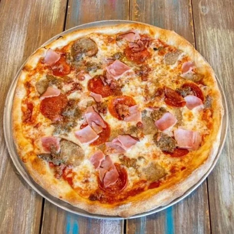 Antonella's Pizzeria's meat lover's pizza, topped with pepperoni, ham, and sausage, on a wooden table.