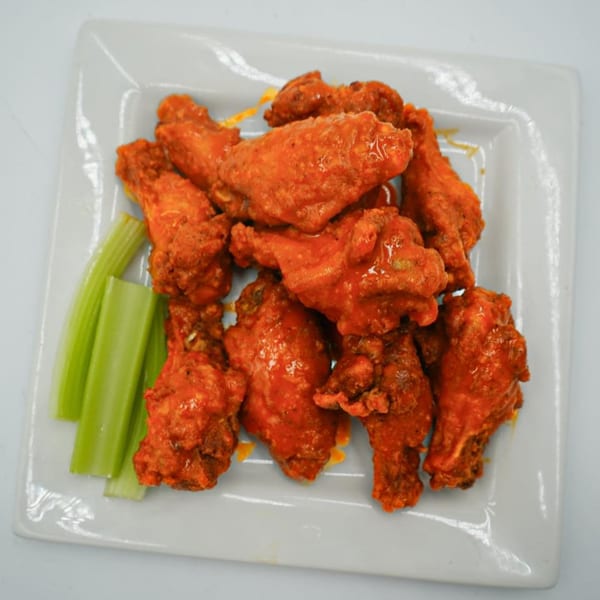 Antonella's Pizzeria Fairbanks' buffalo wings, coated in red sauce, served with celery sticks on a white plate.
